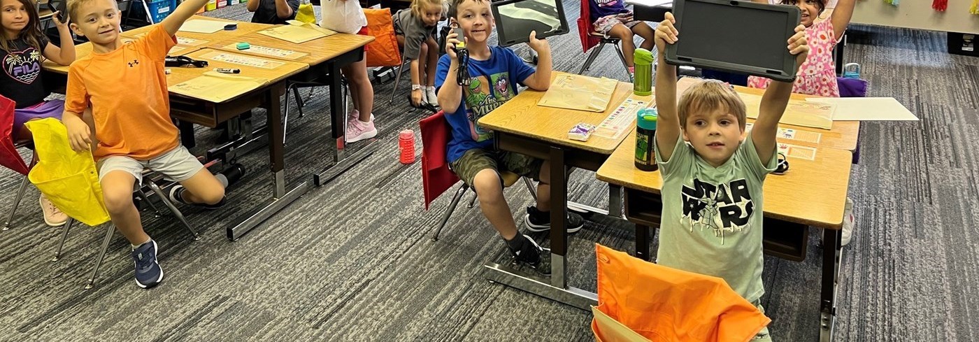 Elementary students holding up Chrome tablets