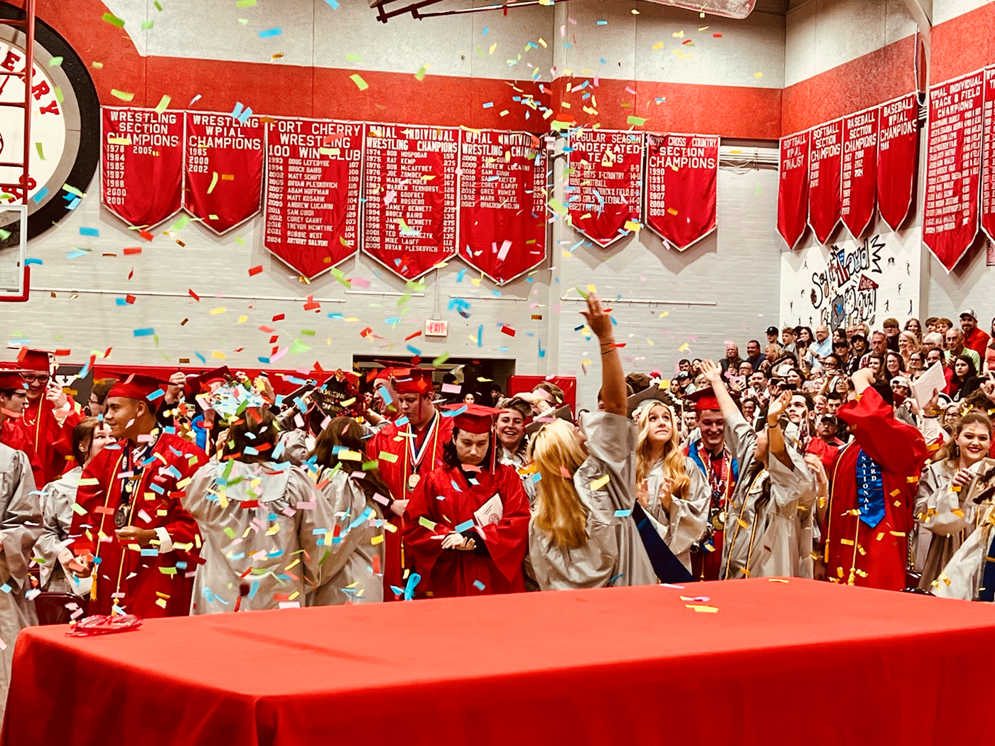 Graduates wearing red and white gowns with confetti in the air